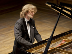 Flyygelin avonaisen kannen takaa näkyy pitkähiuksinen mustapukuinen nuori mies soittamassa pianoa. Kuva Jyväskylä Sinfonia